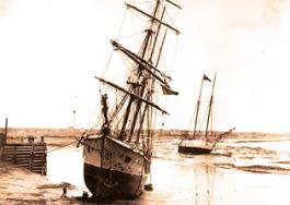 Before: small 1908 photo of sailing ships at low tide on a river